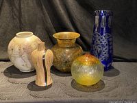 Five vases of various materials and shapes displayed together on black fabric background, showing all five items in the lot