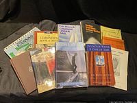 Photo showing 11 sailing books laid out together on a dark surface, titles include Cruising Under Sail, Alone at Sea, and A Unit of Water, A Unit of Time.