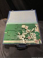 Open blue box containing green and white Mah Jong tiles arranged mostly flat with some scattered.