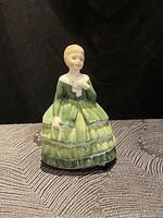 Front view of Royal Doulton Belle figurine wearing green tiered dress and holding a white object.