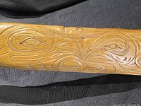 Close-up image showing detailed indigenous design featuring carved eye and abstract shapes in Salish style on the paddle shaft.