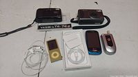 Overview of all items: two cameras, iPod Nano, earphones, charging cable, LG and Motorola phones