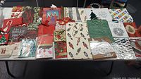 Multiple Christmas gift bags placed on a table showing various patterns and designs including trees, snowmen, and holiday greetings.