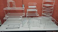 Full view of all white wire closet organizing racks and shelves displayed on table against red wall.