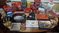 Photo showing multiple collectible tin containers arranged on a table, featuring a wide variety of shapes, sizes, and colorful vintage designs.
