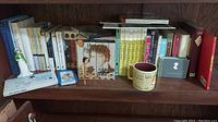 Shelving with multiple Jane Austen books, a figurine, a mug with Jane Austen quotes, a disc in a blue case, and boxed DVD or VHS movie sets