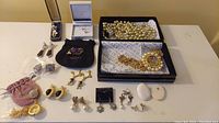 Wide shot showing all assorted jewelry spread out on a surface including earrings, a large amethyst pendant, multiple chains, and other costume pieces.