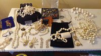 Overview of lot including pearl necklaces, earrings, charms, and costume jewelry pieces on a white surface