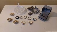 Display of all rings arranged with metal ring sizer and clear glass dish on table.