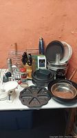 Photo showing assortment of kitchen items including knives, mixing bowls, baking pans, grinder, and strainer bowl