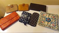 Seven assorted lady's wallets and a fabric case with floral embroidery placed on a white surface.