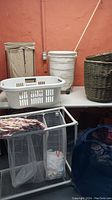 Full view of all laundry bins and baskets on and around table including plastic basket, collapsible bin, wicker basket and rolling hamper.