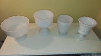 Four milk glass pedestal bowls and vases arranged in a row showing shapes and styles