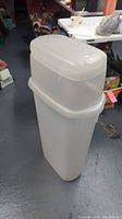 Full view of the tall, white Rubbermaid gift wrap storage bin on floor with lid.