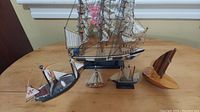 Full view of all five sailing ship models arranged on a wooden surface, showing different sizes and styles including detailed tall ship and wooden sailboat.
