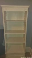 Front view of the tall white bookcase showing four shelves and drawer.