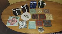 Overview of all tiles and coasters spread on table showing variety of colors, designs, and materials, including stacked dark coasters tied with white ribbons and decorative ceramic tiles.