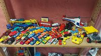 Wide view of toy vehicles arranged on a shelf showing the variety of cars, trucks, and helicopter.