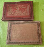 Two antique comic books by Rodolphe Topffer, one with a red cloth cover and gilt illustration, the other with a tan cover and decorative borders.