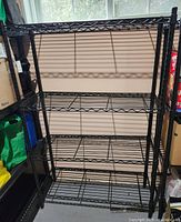 Front view of one black metal wire shelving unit with four shelves against a wall