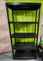 Front view of one assembled black plastic shelving unit showing five vented shelves and tubular supports.