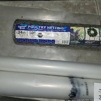 Close up of unopened roll of 1 inch poultry netting chicken wire, 24in x 50ft, Garden Zone brand, alongside white Polytarp Super 6 roll.