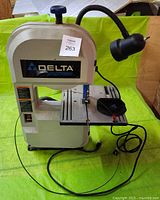 Full front view of Delta ShopMaster BS100 band saw showing attached adjustable worklight, cutting table with blade guard, power cord, and base.