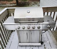 Full front view of stainless steel 5 burner propane BBQ grill with side burner and closed lid, showing control knobs and storage cabinet.