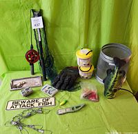 Photo showing Fenwick folding net with telescopic handle, fishing signs, fish scaler, wire chain stringer and some other small fishing gear on green background.