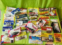 Photo shows a collection of multiple packaged fishing soft plastic and rubber baits from various manufacturers arranged on a green backdrop.