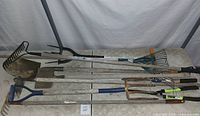 Full view of garden tools laid out on a table including rakes, shovel, scrapper, and fork showing the overall condition and layout.