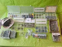 All hardware items displayed on green table surface, showing assortment of screws, rivets, crimps, and small fasteners in boxes, trays, and containers.