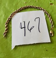 Bracelet laid out on green surface with handwritten tag '467'