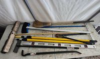 Photo showing 10 large tools laid out including brooms, bolt cutters, painter poles, T-square, level, magnetic broom, and crowbar.