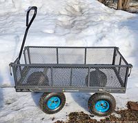 Photo showing metal gray Yardworks garden wagon with mesh sides, blue rims on pneumatic tires, and pull handle in an outdoor setting with snow in background.