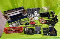 Wide view of assorted drill bits, driver bits, hole saws, sanding drums, wire brushes, and related accessories spread on green surface.