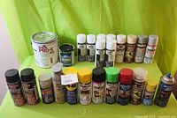 Various cans of paint and spray products arranged on a green surface against a green backdrop, showing brands like Kilz, Tremclad, WD-40, Rustoleum, Dupli-Color, Armor Coat, and others.