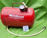 Red MotoMaster air tank shown on green tarp, includes tank, handle, white hose, and pressure gauge visible