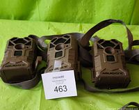 Three Muddy trail cameras in camouflage pattern with grey mounting straps, all shown front-facing.