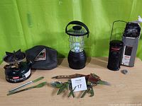 Photo of camping stove with cutlery and pouch, hand crank LED lantern, and Coleman propane lantern in original box with accessories.