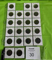 Twenty-one large cents in individual cardboard flips arranged in rows on green cloth with lot number card