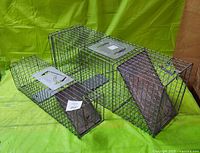 Photo showing two Advantek live animal traps made of metal wire mesh, side by side on green fabric background.