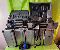 Six silver metal parts tool cases stacked and arranged, showing open interior with black tool platters, foam inserts, and dividers, some with shoulder straps and one with key lock
