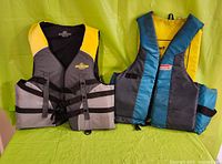 Two blue/yellow buoy-o-boy youth flotation vests and one teal/black/yellow coleman flotation vest.