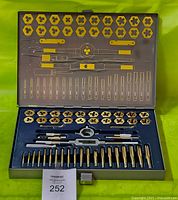 Open metal case showing an organized set of taps, dies, and handles arranged in blue foam with yellow highlights for tool positioning and sizes displayed on the inside of the lid.