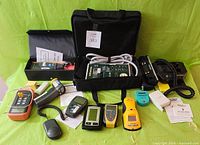 Photo showing the full range of test equipment laid out on a green background including analyzers, meters, testers, and their manuals.