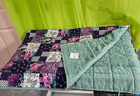 Quilted throw blanket with patchwork floral design and solid green back folded showing both sides.