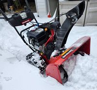 Front-side view of red snow blower in snow showing auger housing and treaded wheels