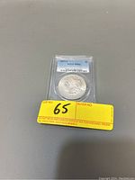 Front view of the 1879-S Morgan Silver Dollar inside PCGS holder with MS63 grade and lot number 65 sticker visible.