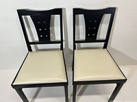 Front view of the pair of Leg O Matic folding chairs showing black lacquer frame and eggshell upholstered seats.
